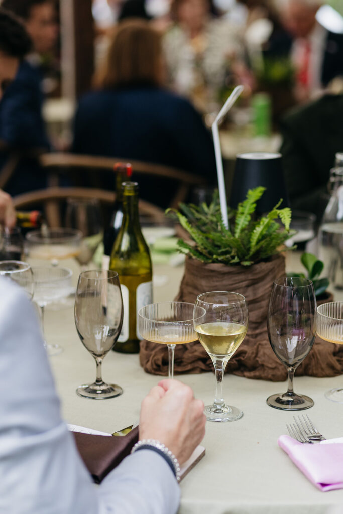 Candid reception table scene with wine glasses and greenery at a house party–style wedding at The Mod House in Ellenville, NY.