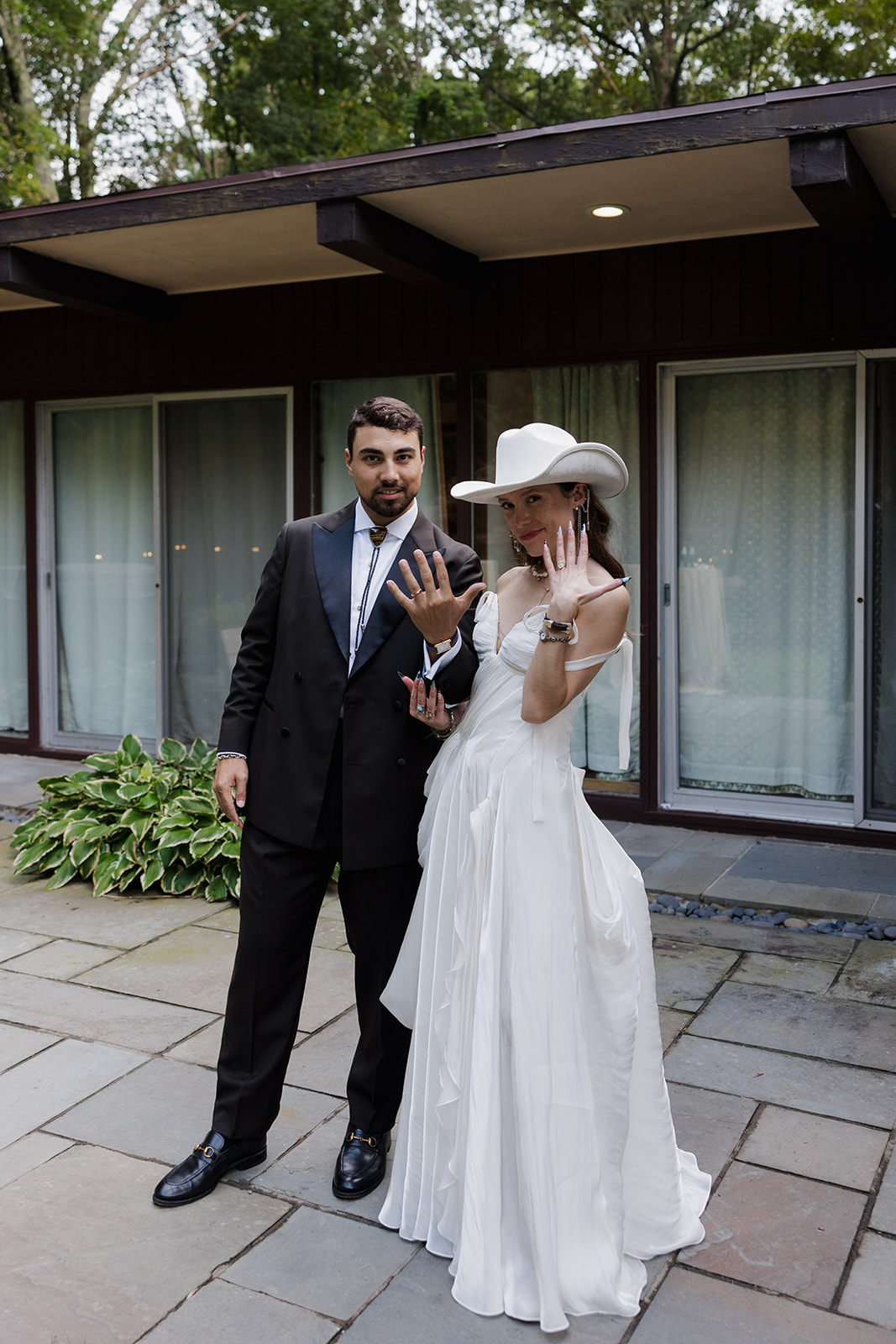 Bride and groom showing their wedding rings while posing outside , a editorial moment.