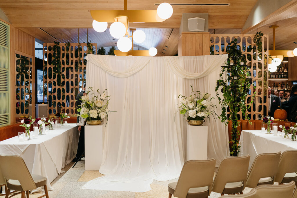 wedding ceremony setup with white linens, green glassware, candles, and modern floral arrangements.