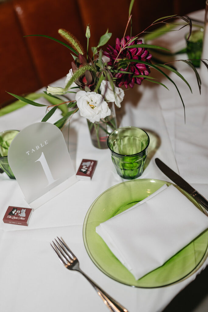 Intimate Acadia NYC wedding table setting with modern florals, green glassware, and minimalist table number design.