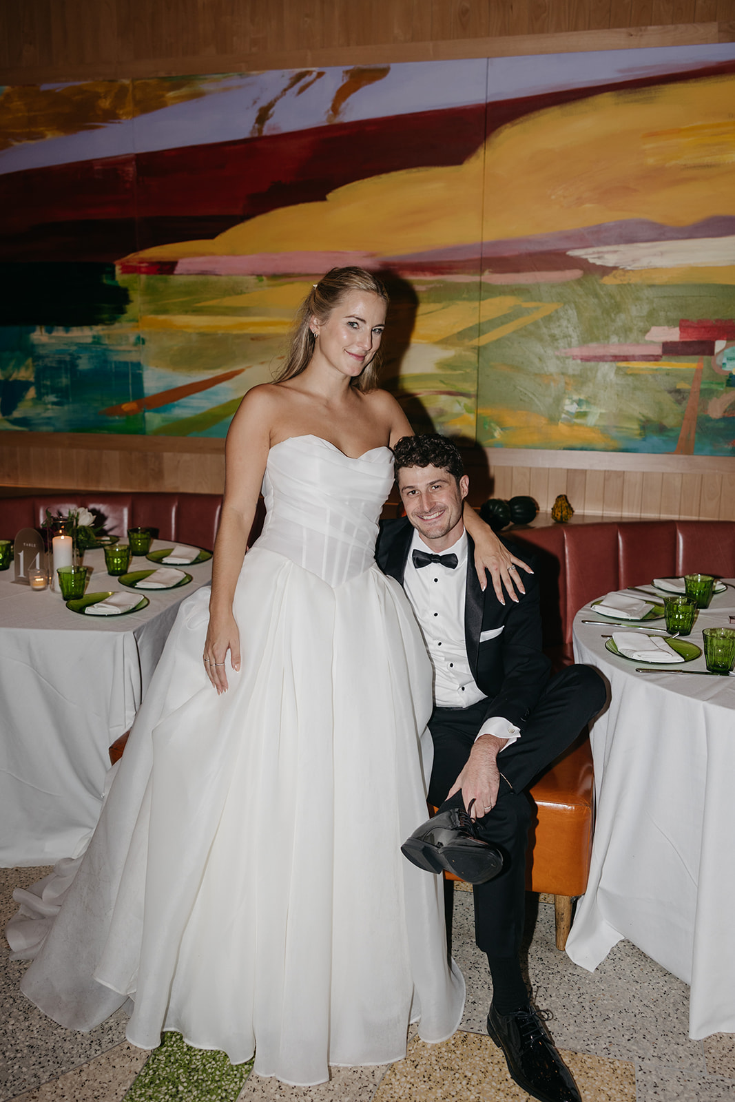 Bride and groom posing inside Acadia NYC surrounded by candlelit tables and colorful modern wall art.