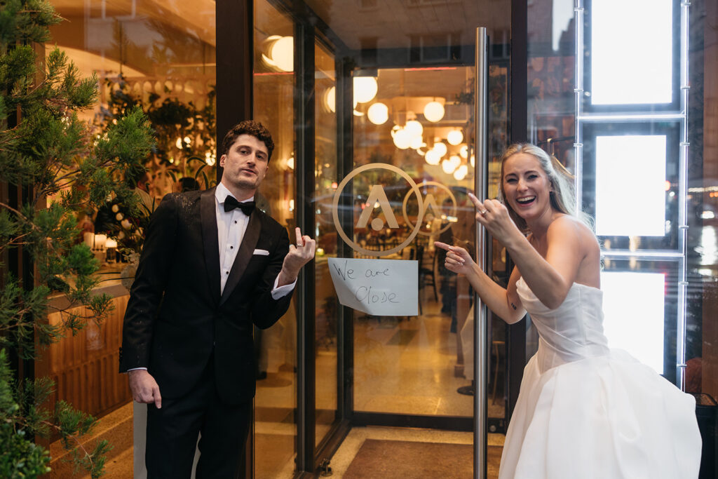 Newlyweds playfully posing outside Acadia NYC entrance after the reception on a rainy New York City night.