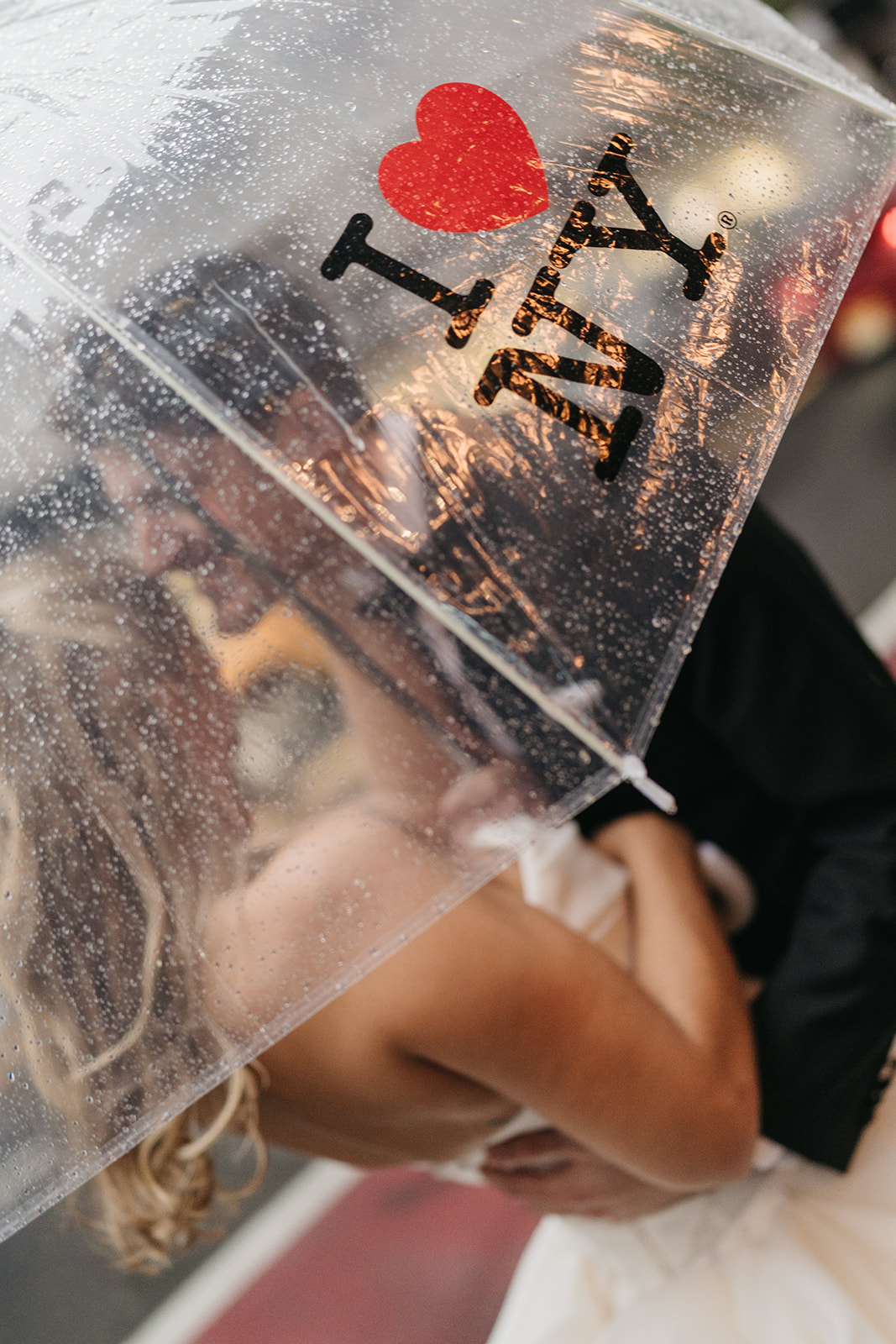 Romantic rainy New York City wedding moment with the couple kissing beneath an I Love NY umbrella.