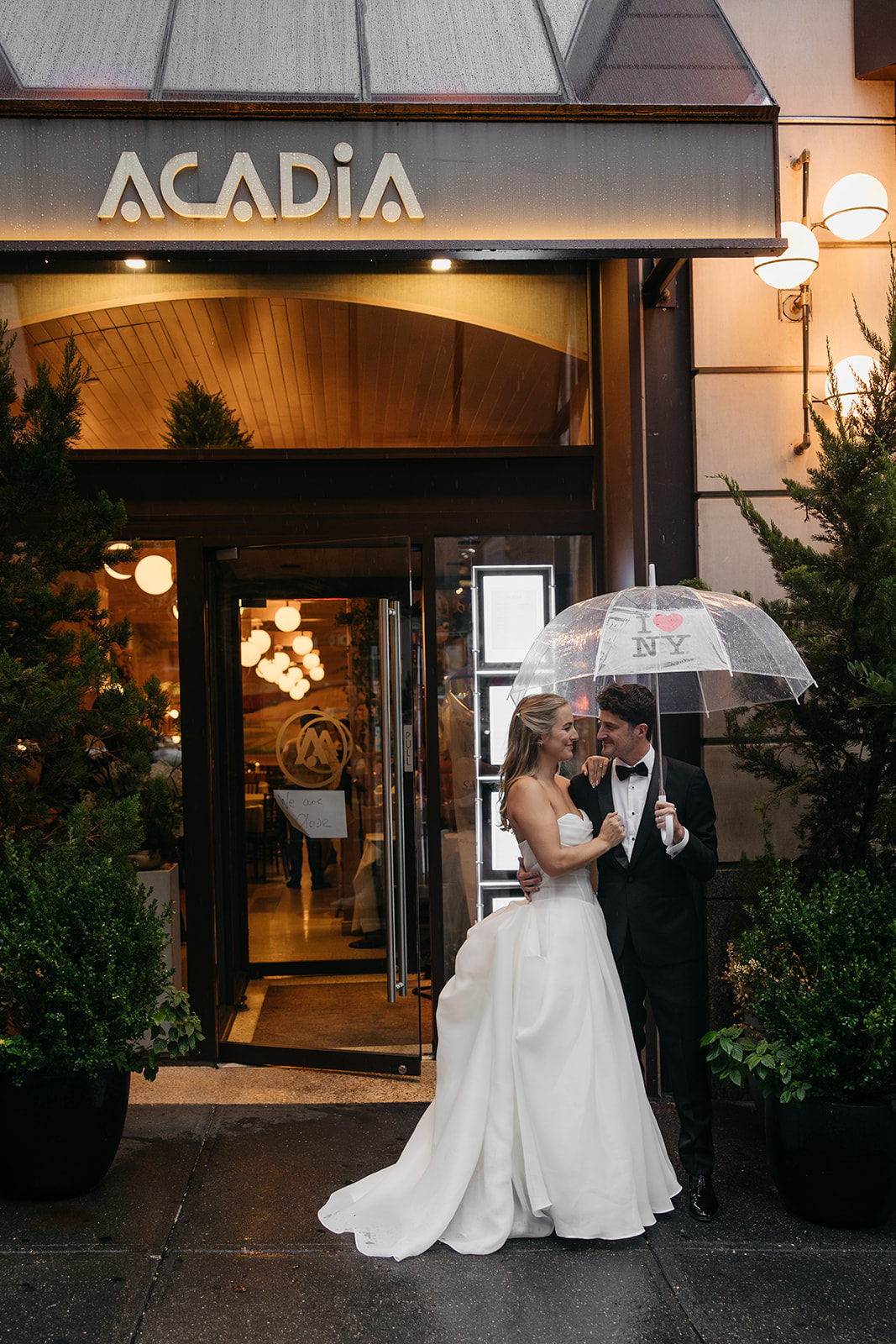 Couple standing outside Acadia NYC entrance at night sharing a quiet moment under an umbrella after the reception.