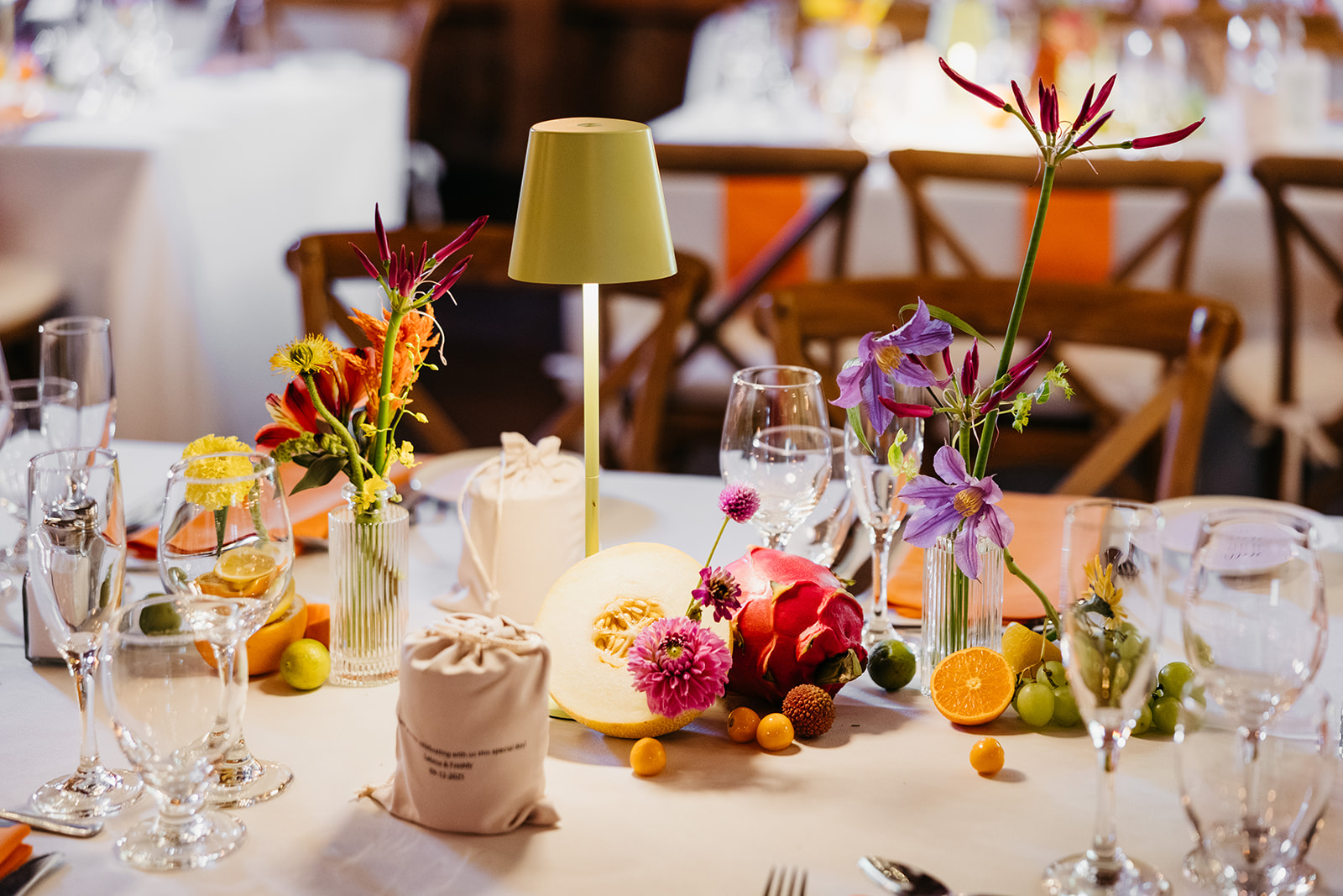 Colorful reception tablescape at The Barns at Wesleyan Hills CT wedding featuring bright florals, dragon fruit, citrus accents, and modern table lamps on white linens.