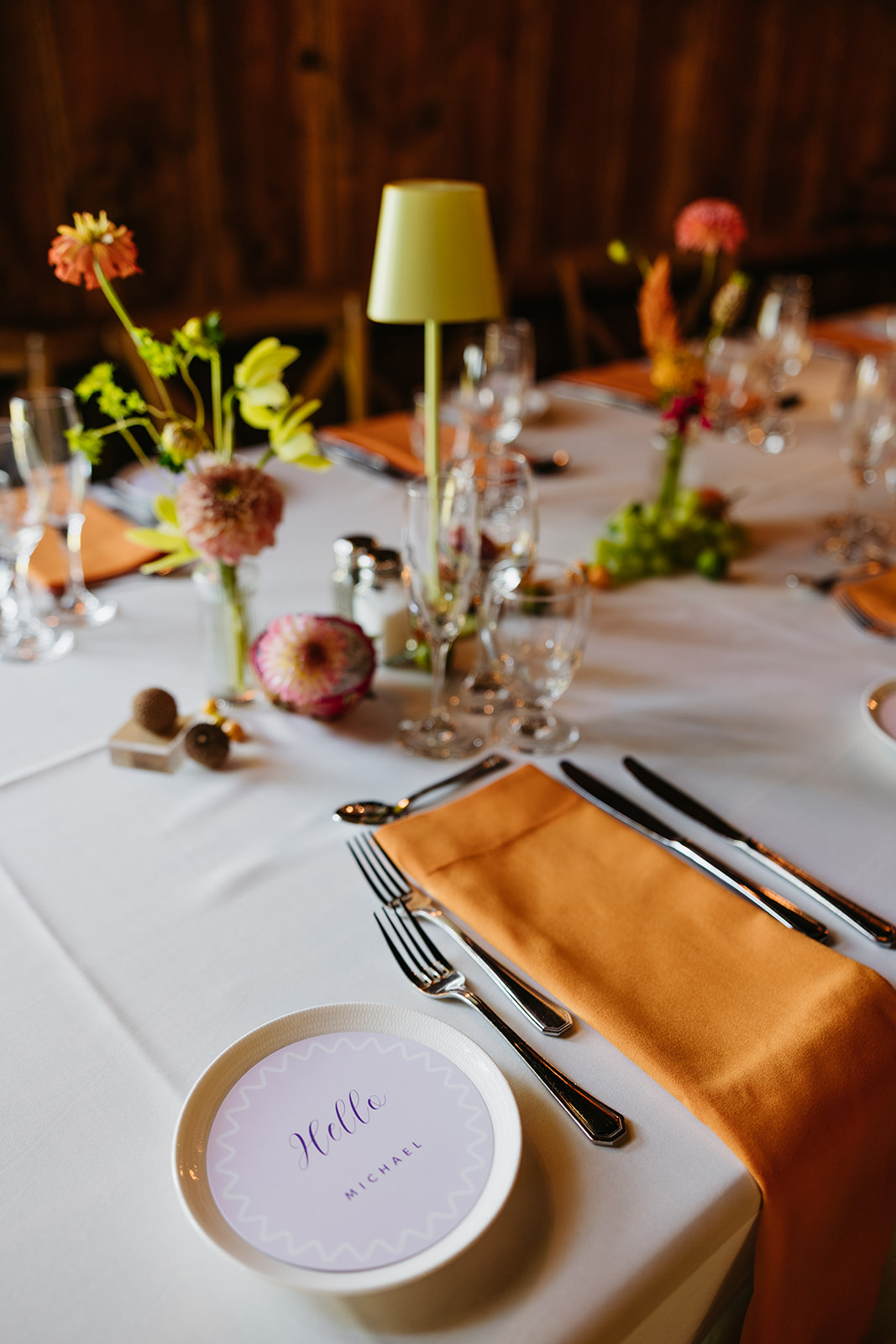 Reception place setting with orange napkin, modern glassware, and floral details during a Connecticut barn wedding at The Barns at Wesleyan Hills.
