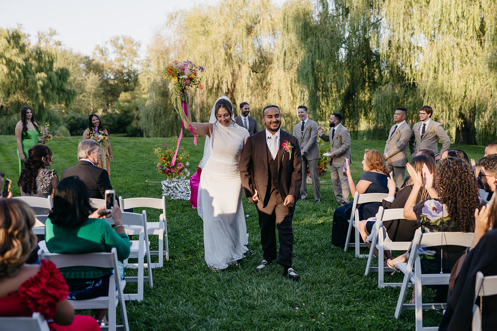 Newlyweds walking back down the aisle at The Barns at Wesleyan Hills CT wedding while guests cheer during an outdoor ceremony.