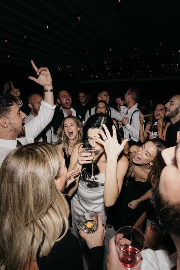 Bride laughing and holding a martini surrounded by cheering guests on the dance floor at a Galleria Marchetti wedding