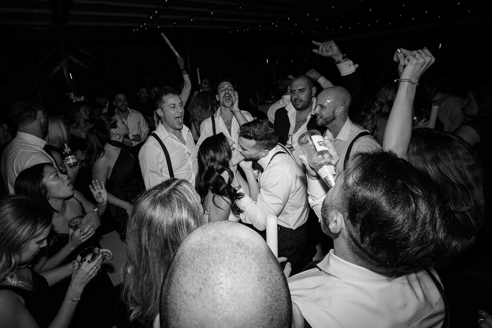 Bride and groom kissing in the middle of a crowded dance floor during an energetic wedding reception
