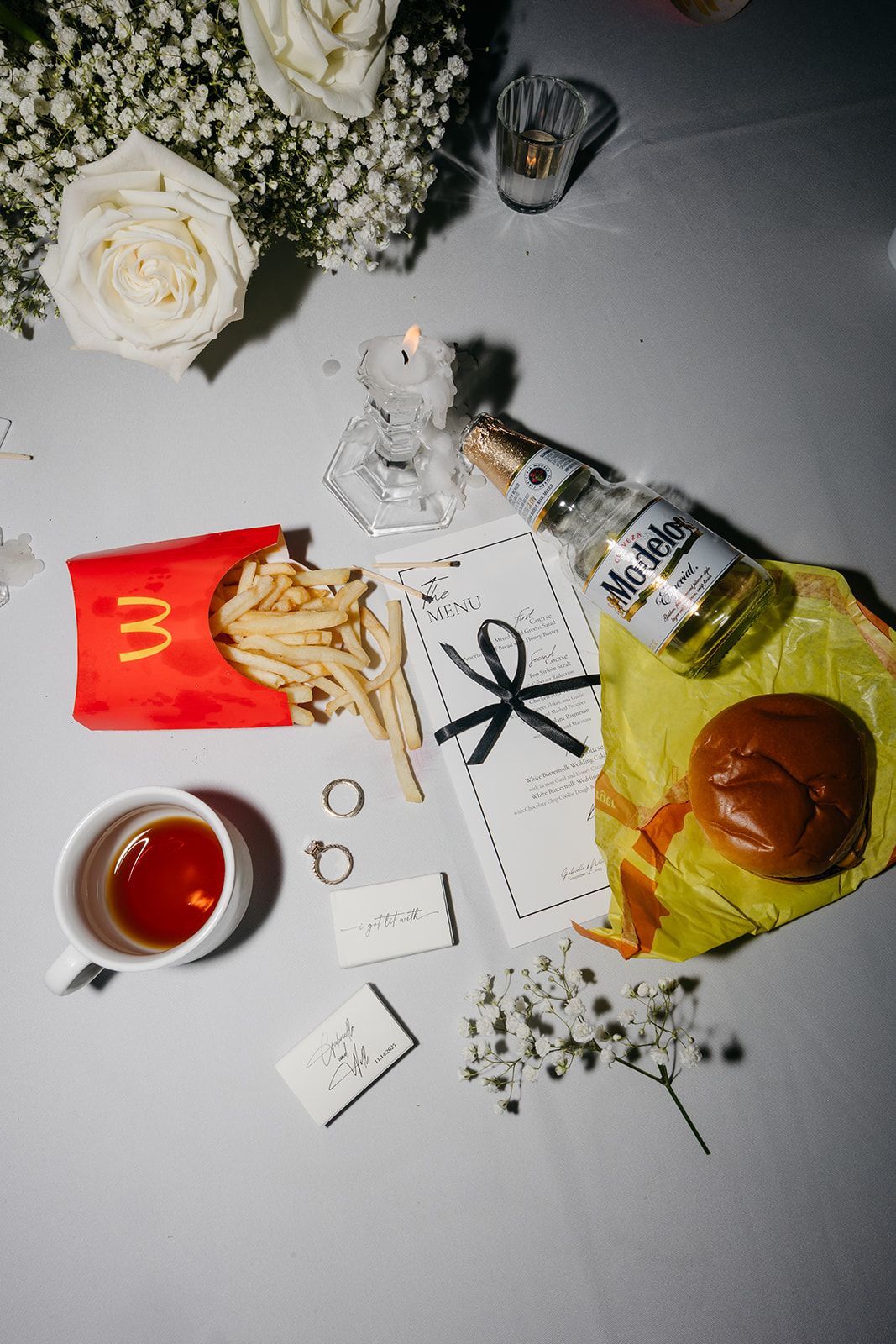 Late night wedding table with McDonald’s fries, burger, and drinks surrounded by candles and floral centerpieces
