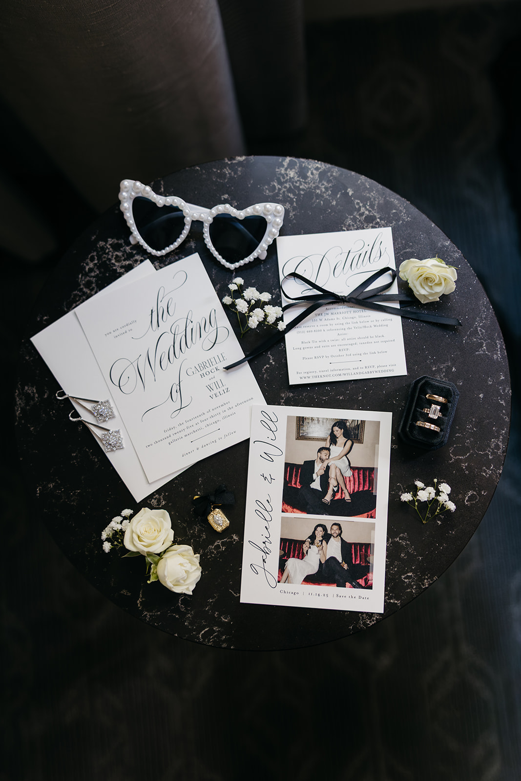 Flat lay of wedding invitations, rings, sunglasses, and stationery styled with elegant black and white details