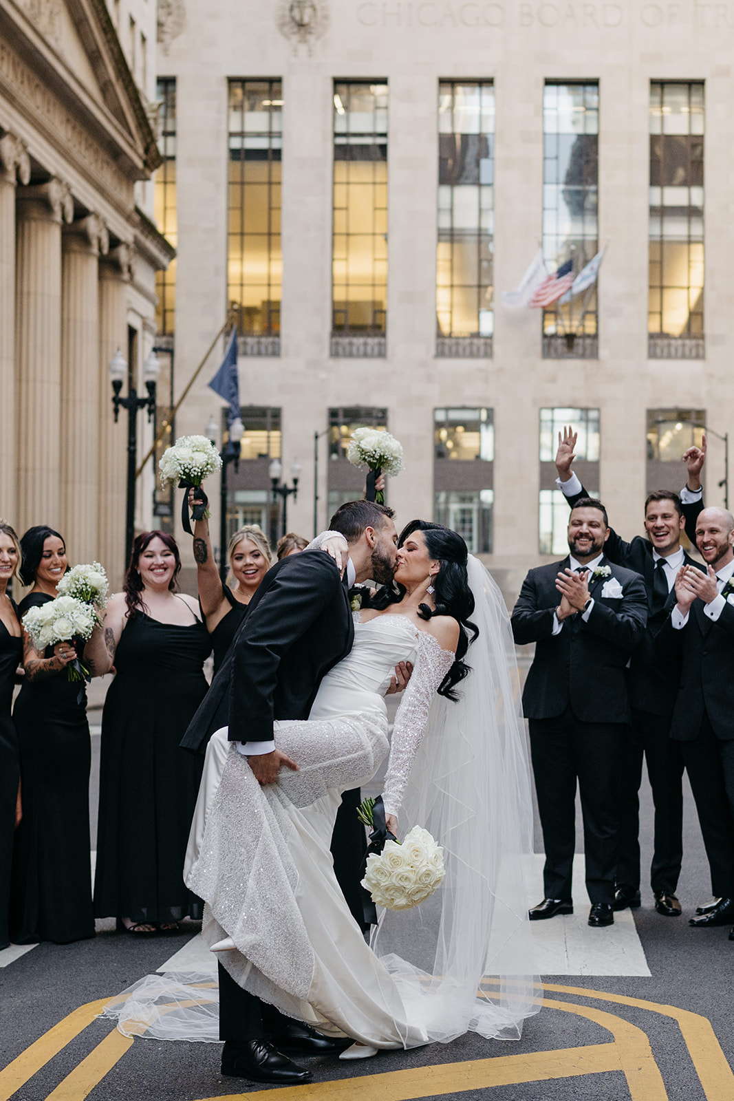 Bride and groom sharing a celebratory kiss in the street surrounded by their wedding party in downtown Chicago