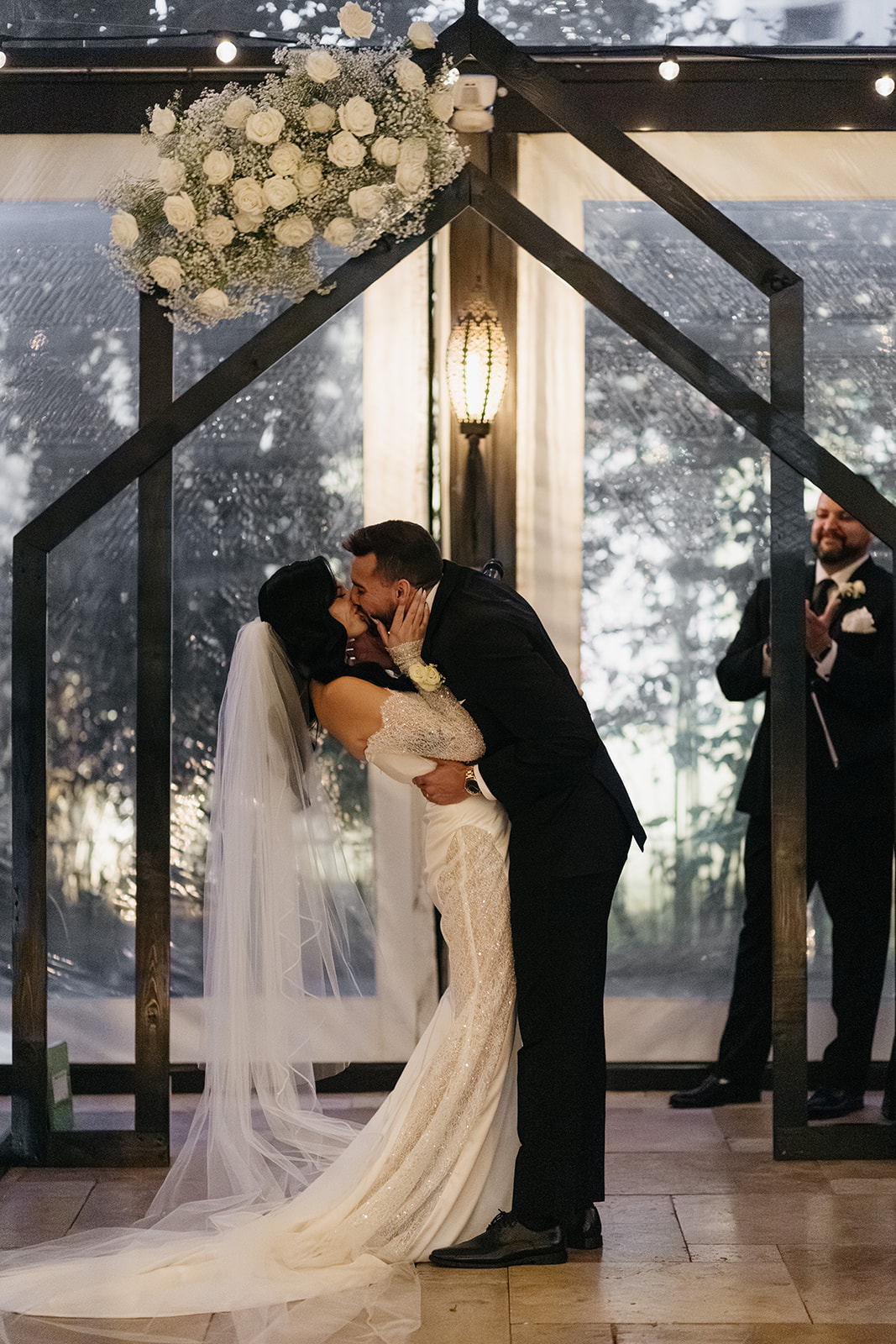 Bride and groom sharing their first kiss during their ceremony beneath a floral arch