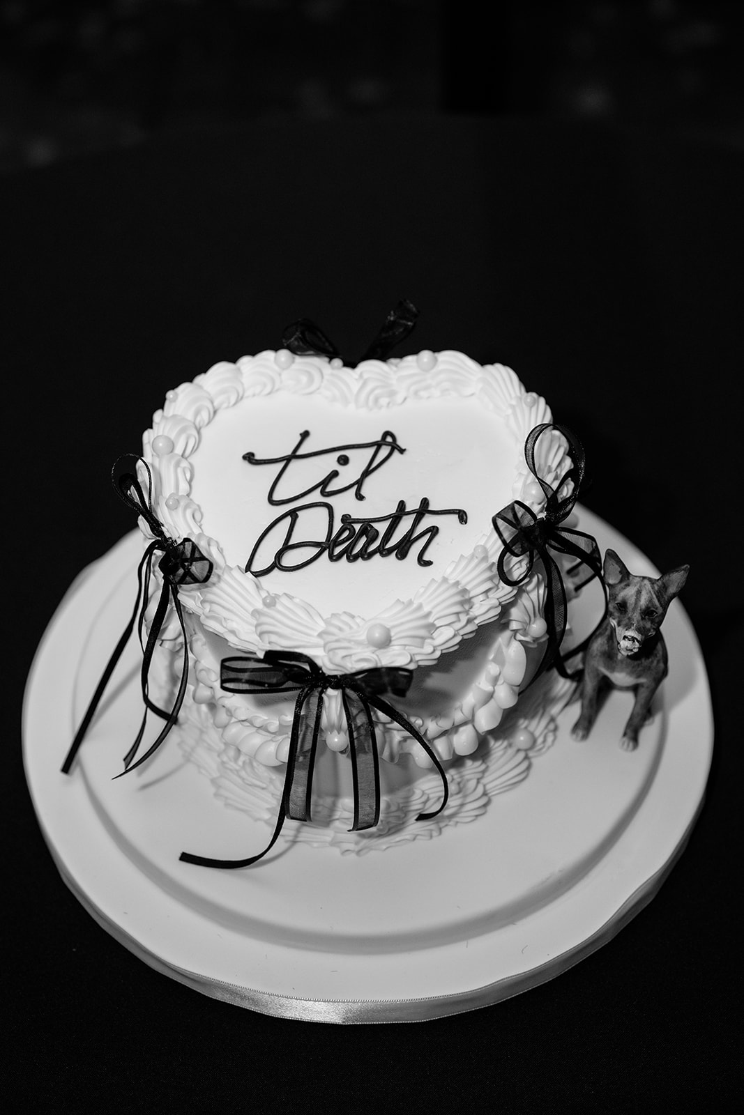 Black and white wedding cake decorated with bows and “til death” lettering at a Chicago wedding reception