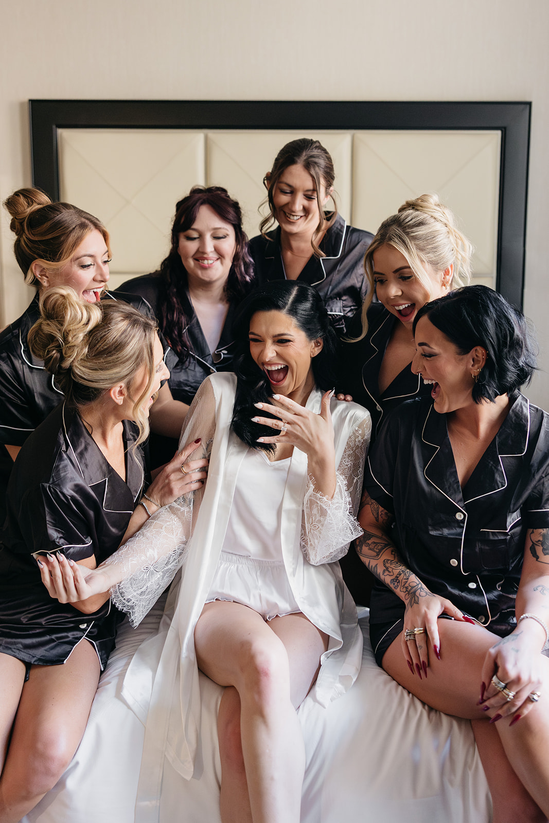 Bride laughing with her bridesmaids in black silk pajamas while getting ready for the wedding day