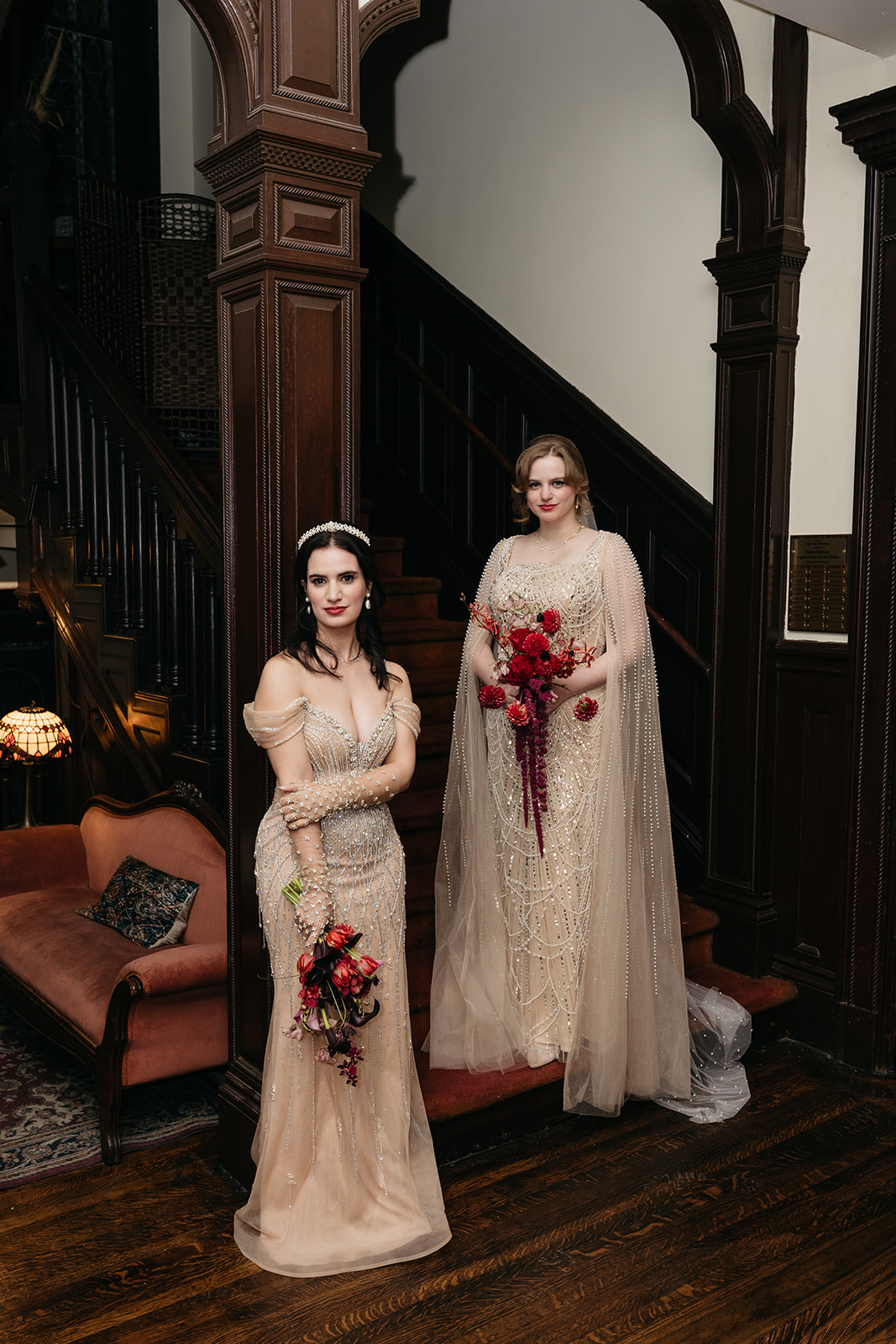 Brides in beaded gowns posing on staircase at Montauk Club NYC wedding with vintage wood interiors
