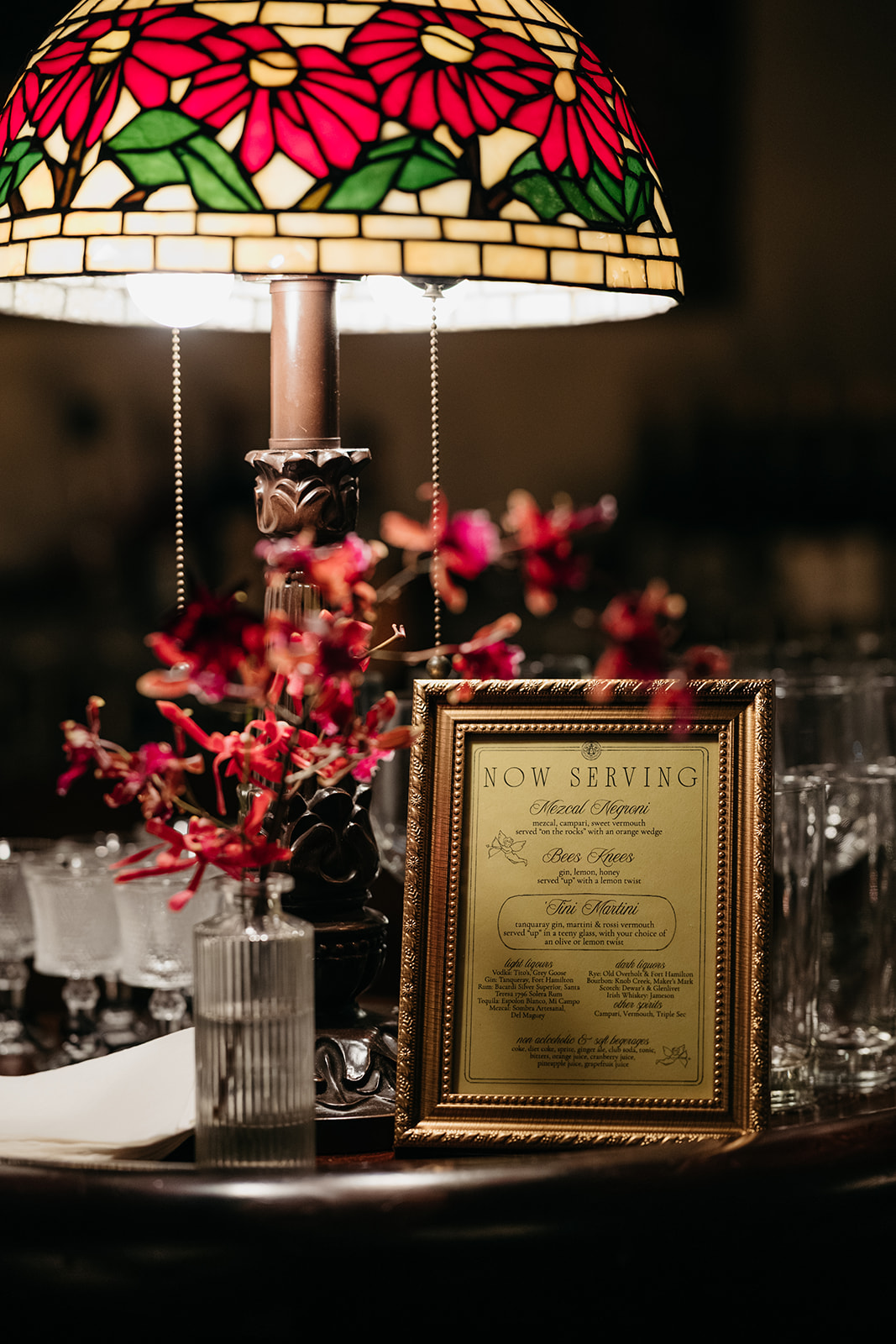 Vintage style cocktail menu display with florals and stained glass lamp at NYC wedding