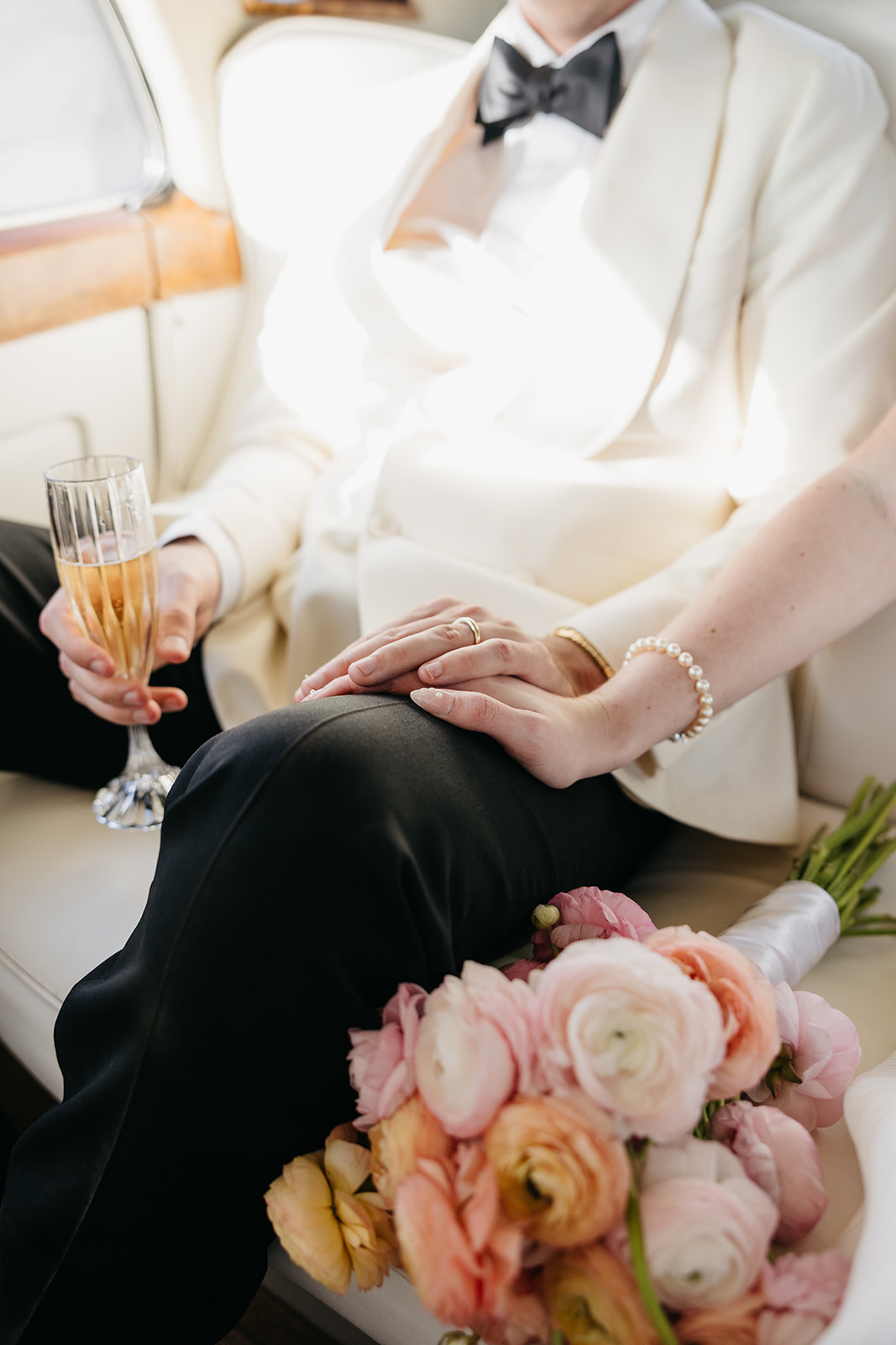 Close up of couple holding hands with champagne and bouquet inside classic car on wedding day