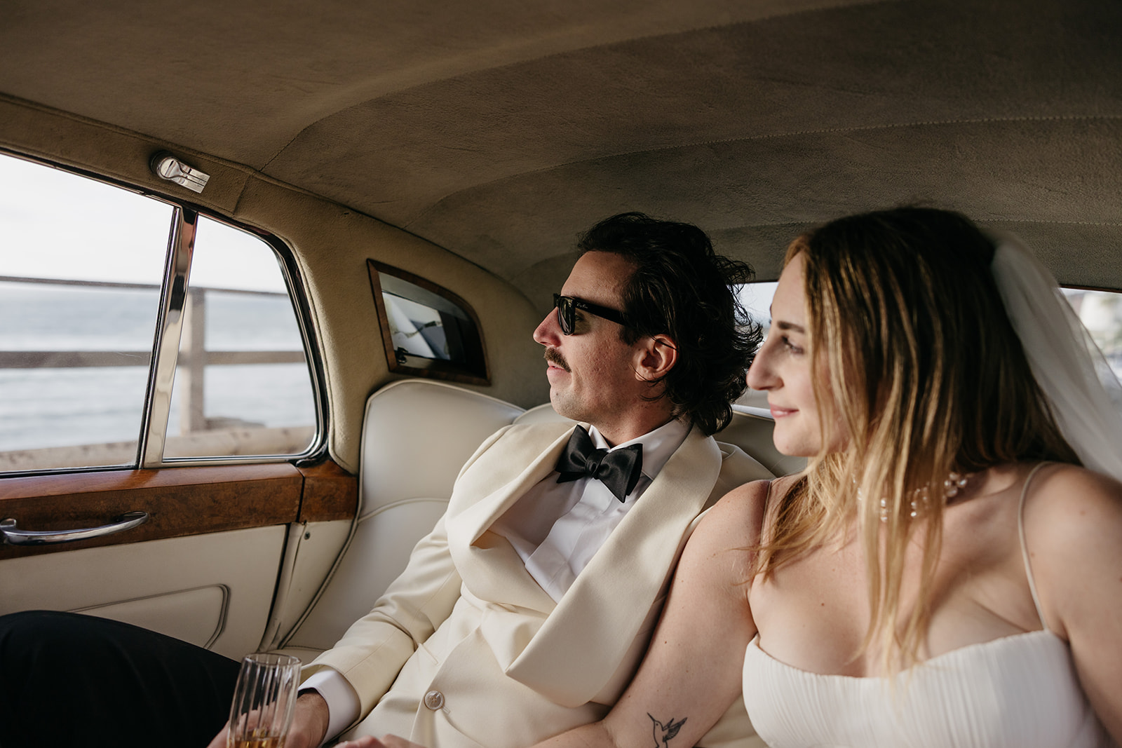Bride and groom riding in vintage car overlooking the ocean after their cliffside ceremony 