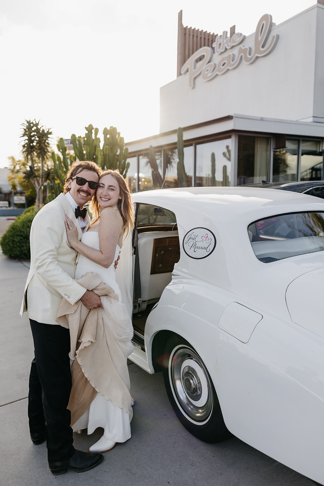 Newlyweds embracing beside vintage car outside the pearl san diego wedding venue with retro sign in background