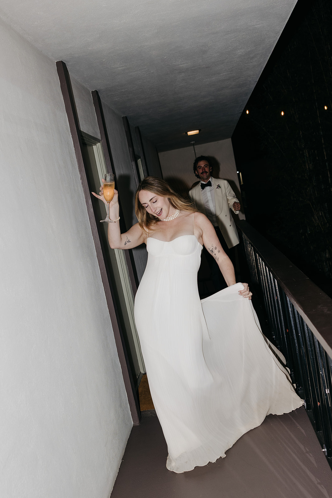 Bride walking hallway holding dress and champagne, candid San Diego wedding photography moment