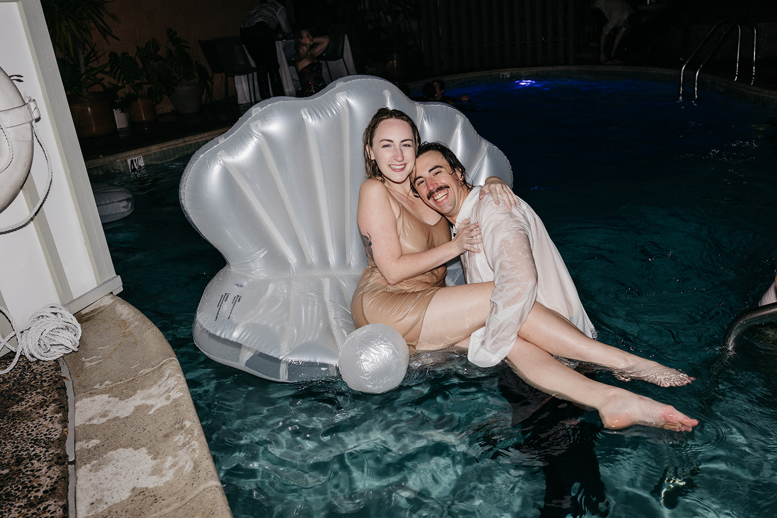 Couple laughing on shell float in pool during fun reception moment at a San Diego wedding venue