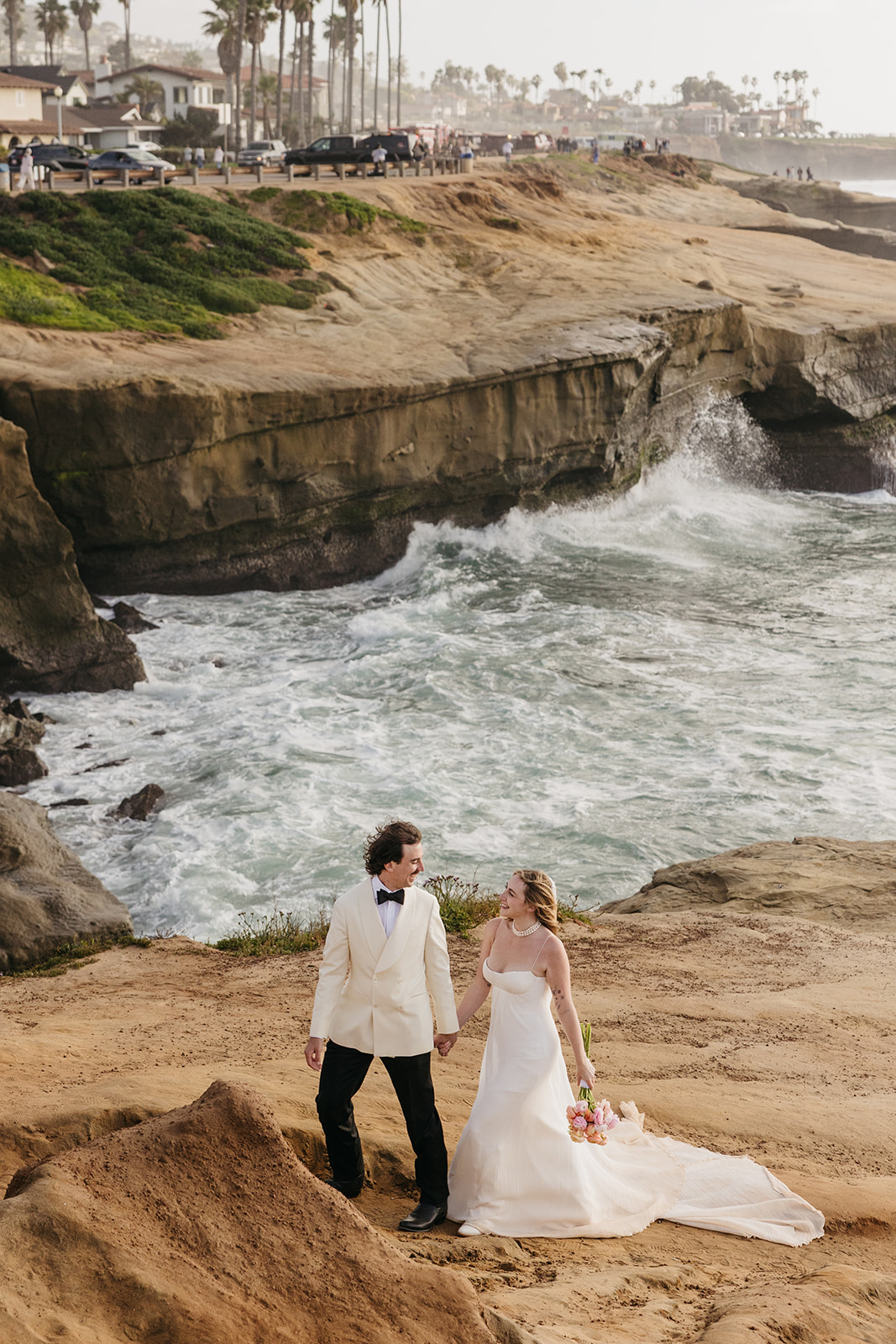 Bride and groom walking along coastal cliffs during the pearl san diego wedding with ocean waves crashing below