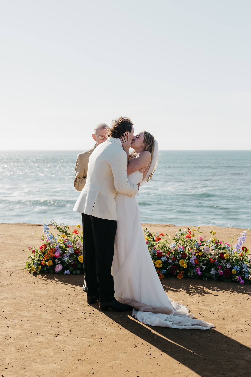 First kiss during outdoor coastal ceremony with colorful florals and ocean view in san diego