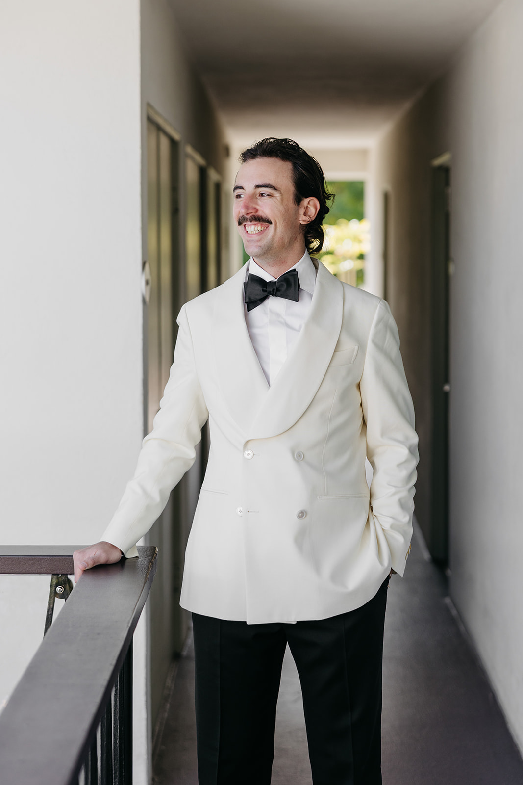 Groom portrait in hallway wearing white tuxedo jacket and black bow tie 