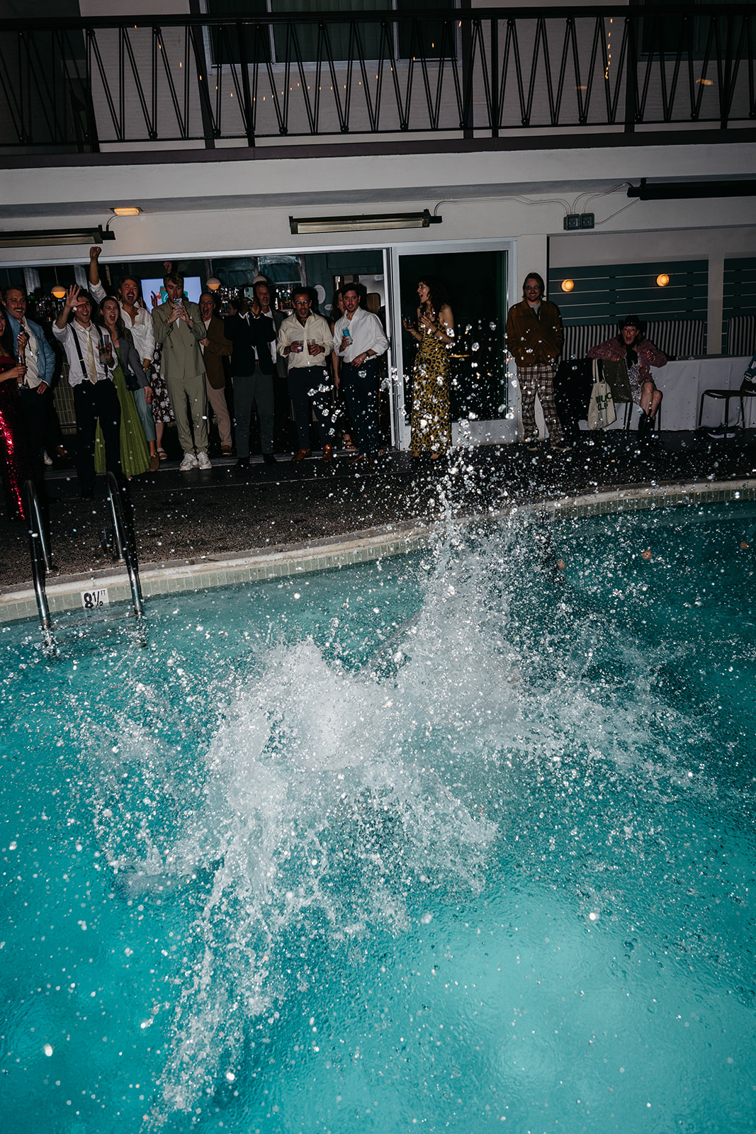 Splash captured mid air as guest jumps into pool, high energy wedding party moment