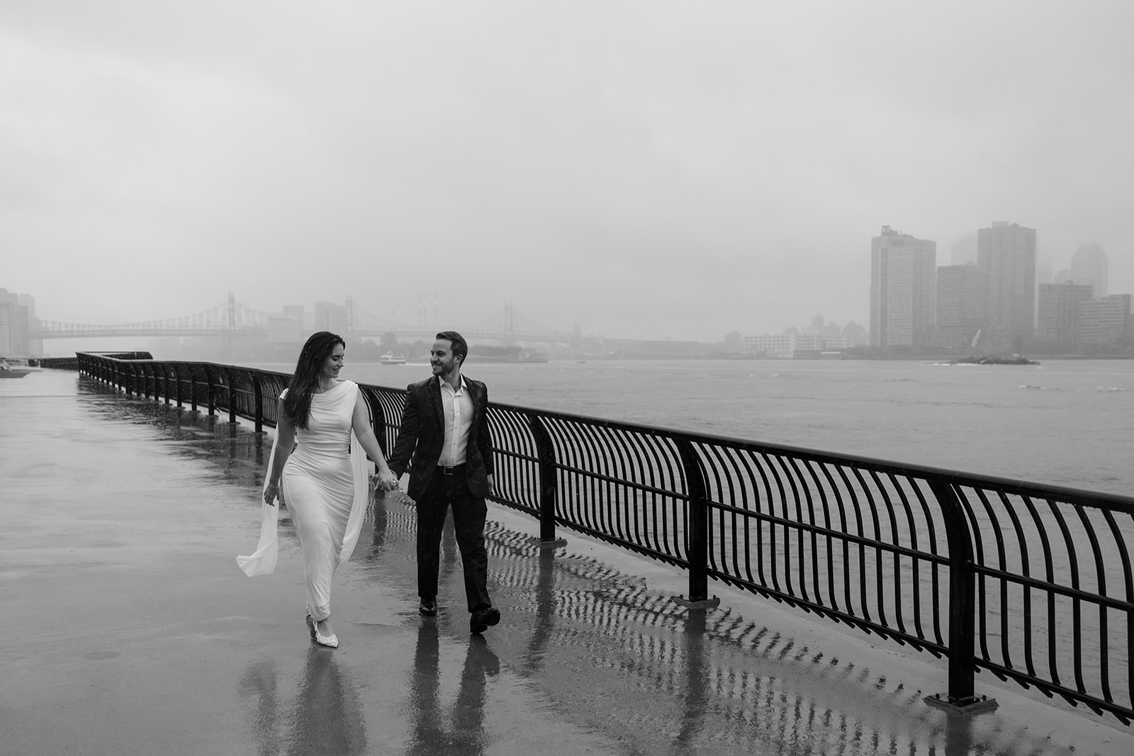A NYC couples walking hand and hand along a riverwalk in the rain