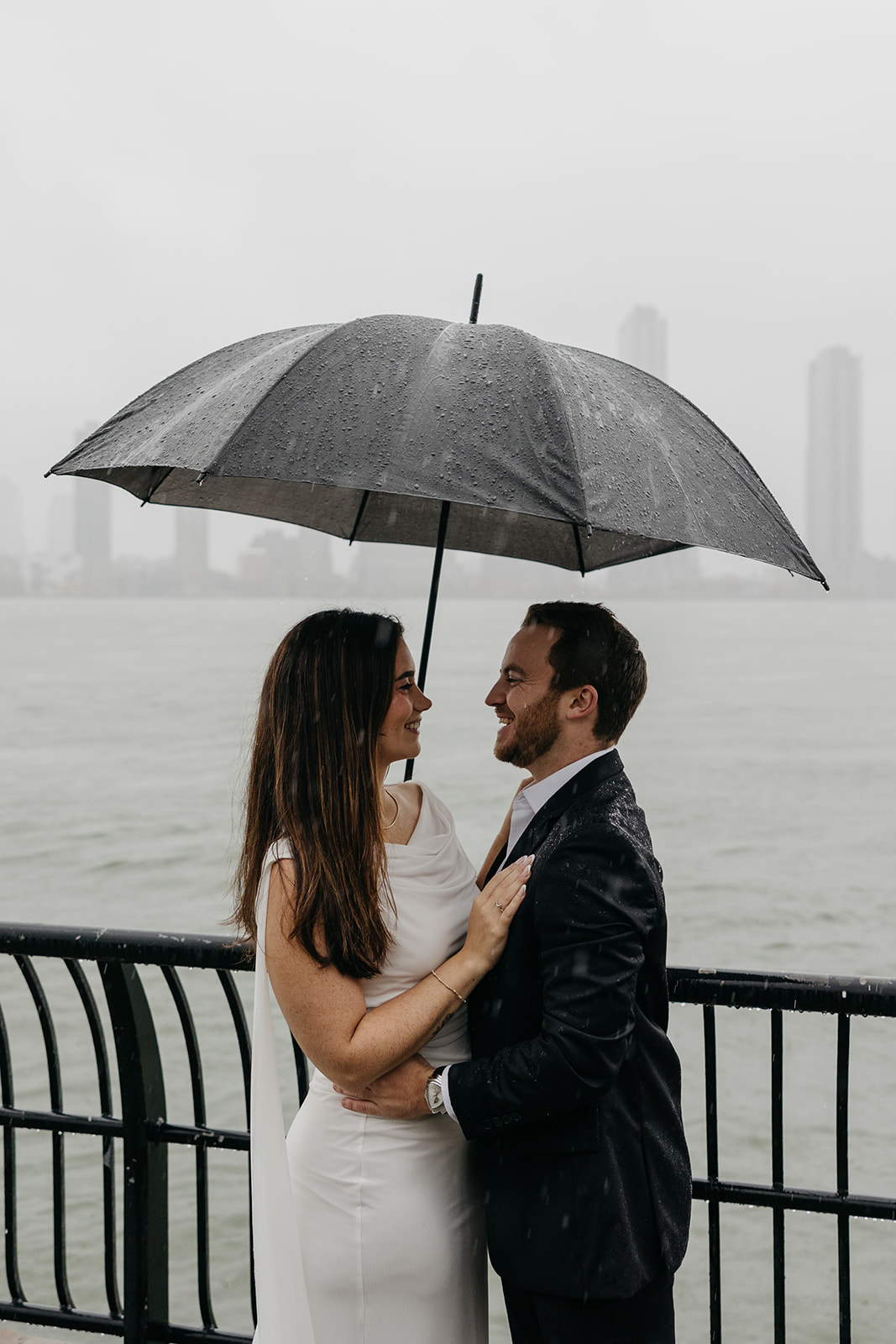 Couple embracing under umbrella during rainy day engagement session in NYC