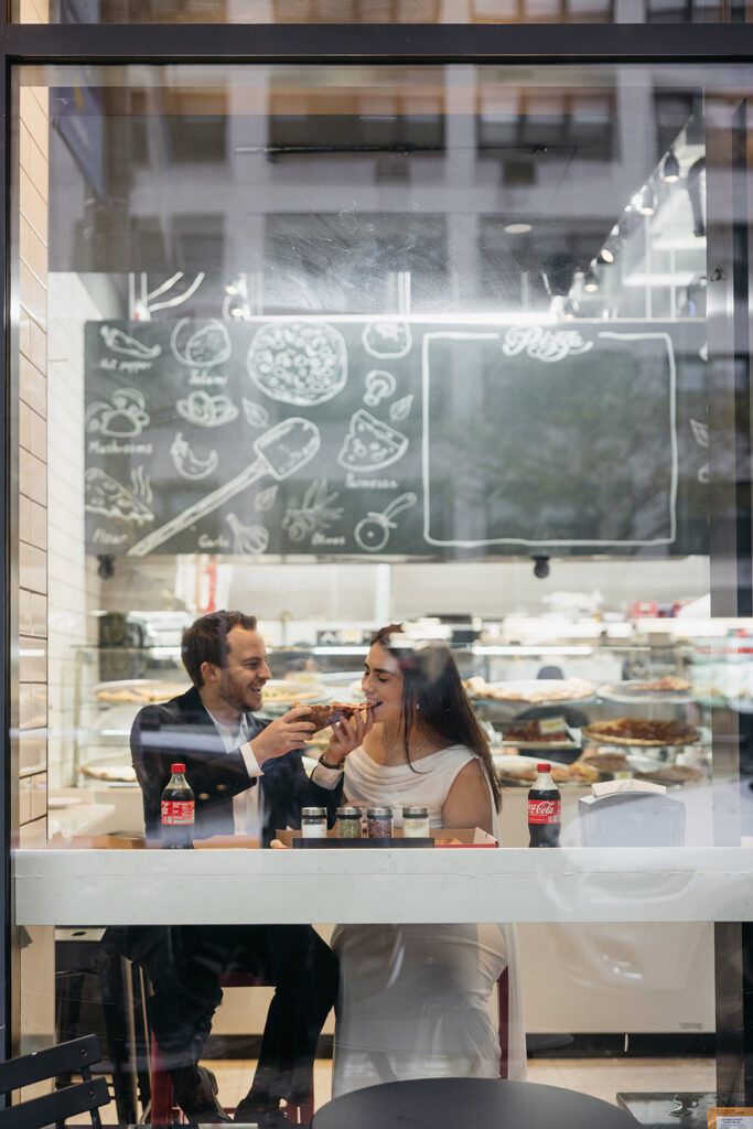 Window photo of NYC couple eating pizza at their favorite spot